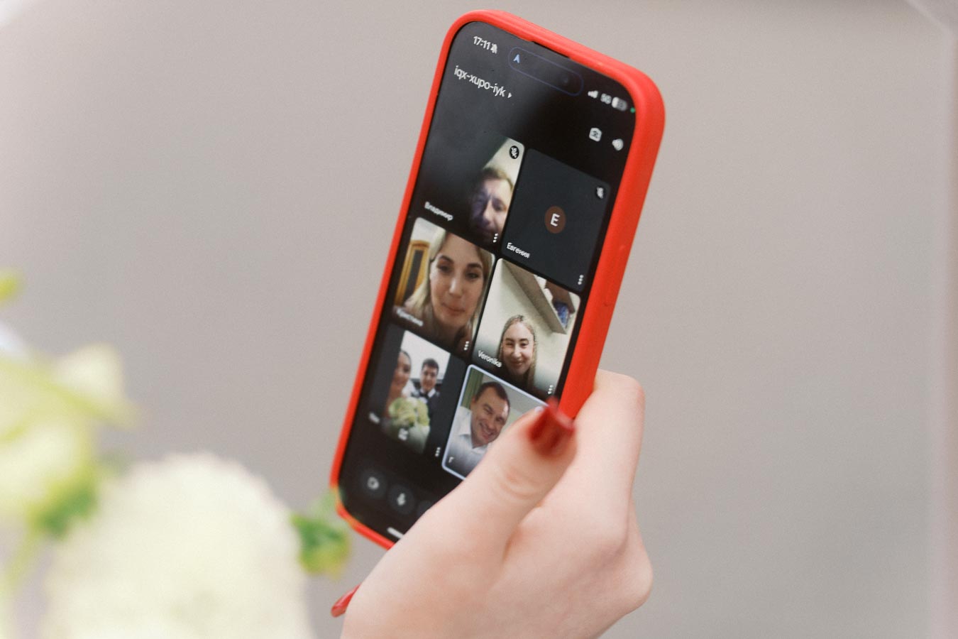 A person holding a smartphone with a red case, engaged in a group video call with several people displayed on the screen.