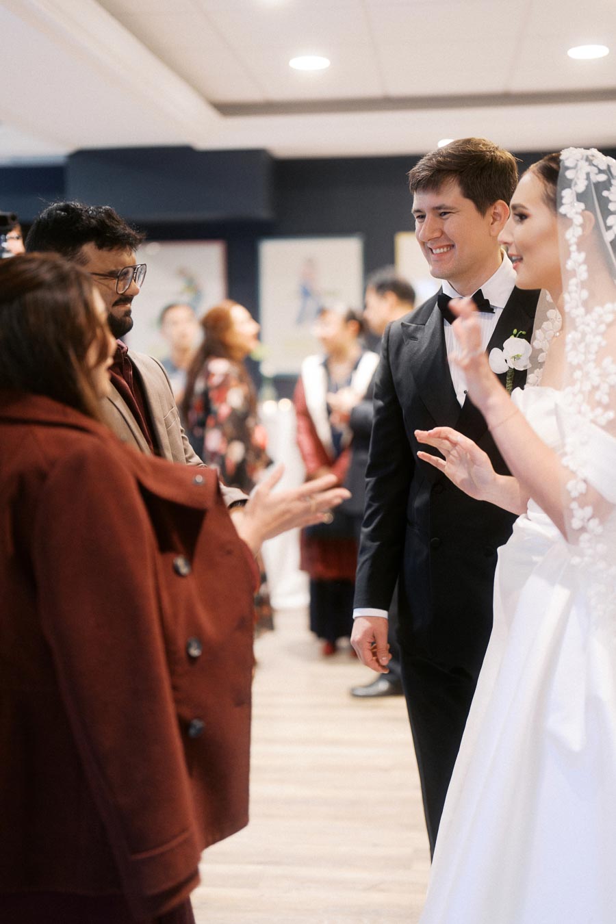 Bride and groom in formal attire smiling and greeting guests at a wedding reception.