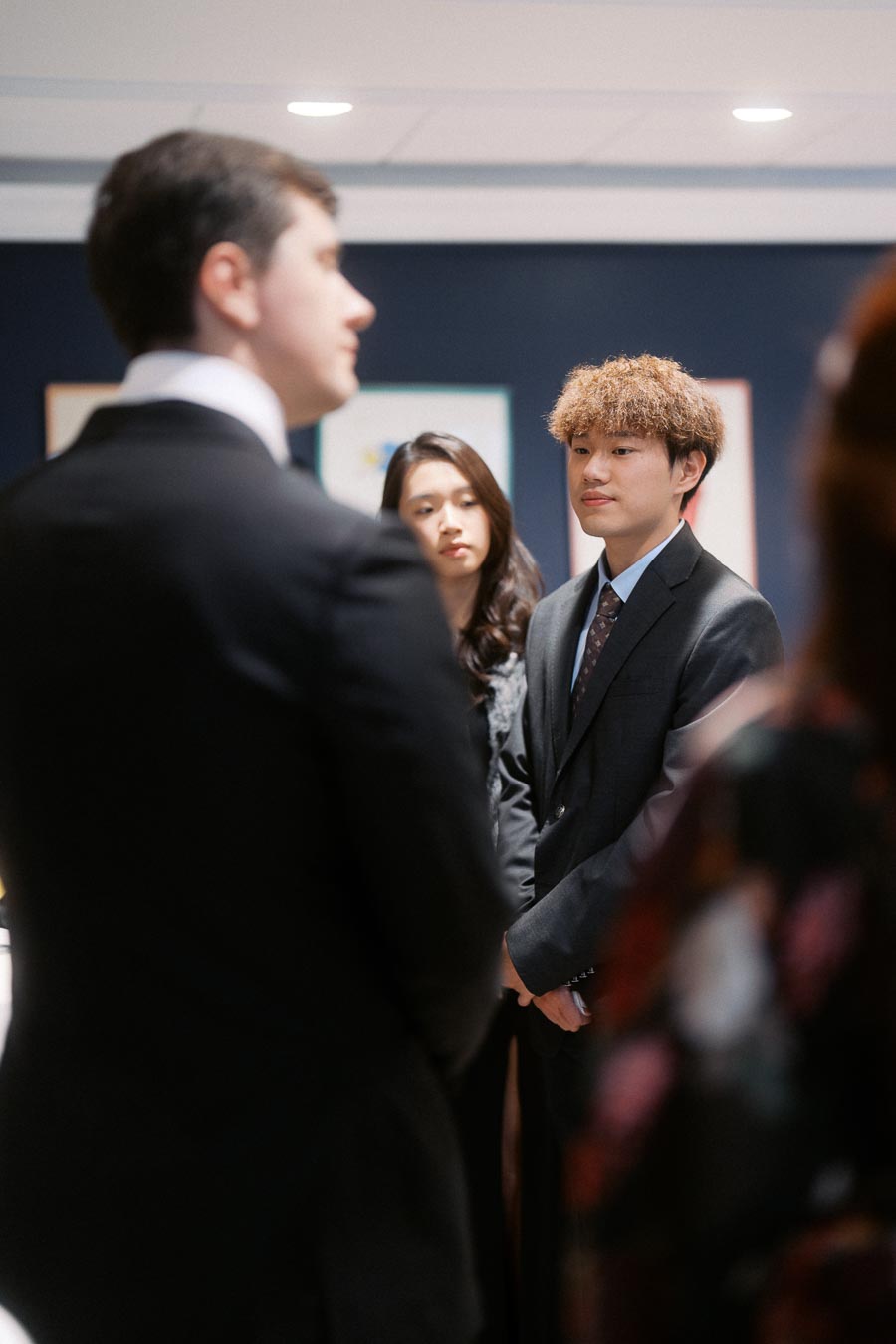 A group of people in formal attire engaging in a conversation during a networking event, with a focus on a man in a suit and tie.