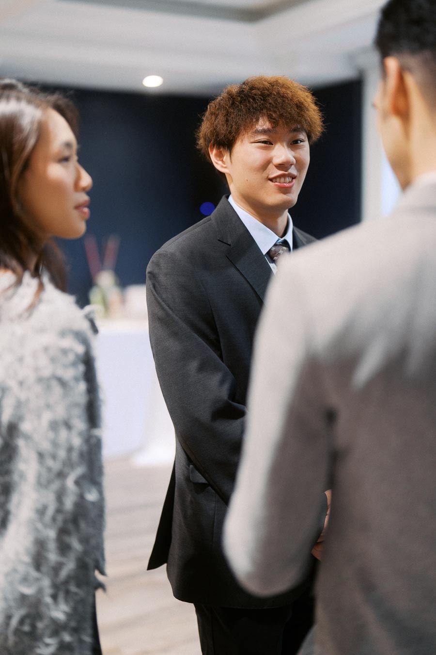 A young professional in a suit smiling and engaging in conversation at a business networking event.