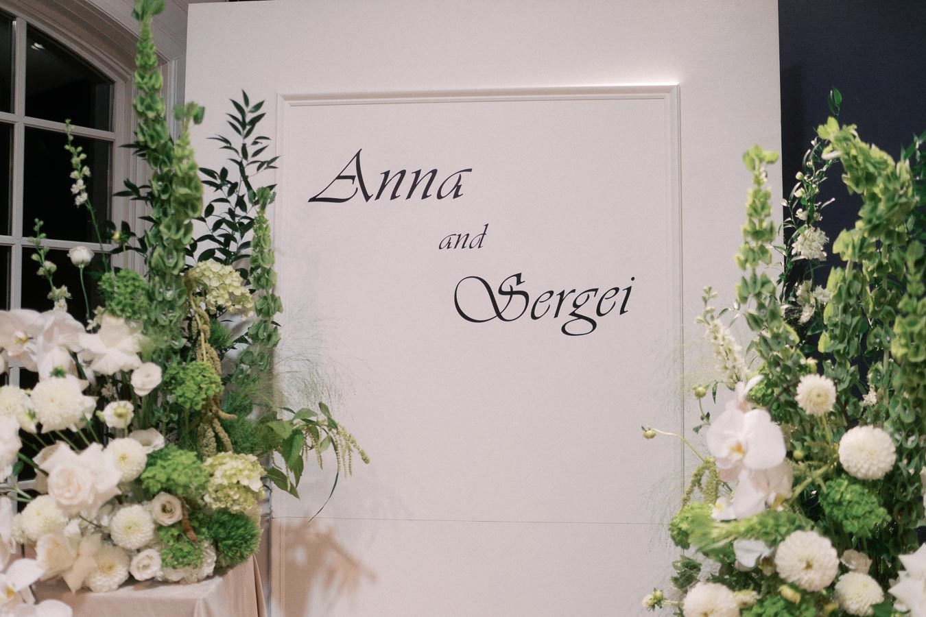 Elegant wedding backdrop with the names 'Anna and Sergei' adorned with lush green and white floral arrangements.