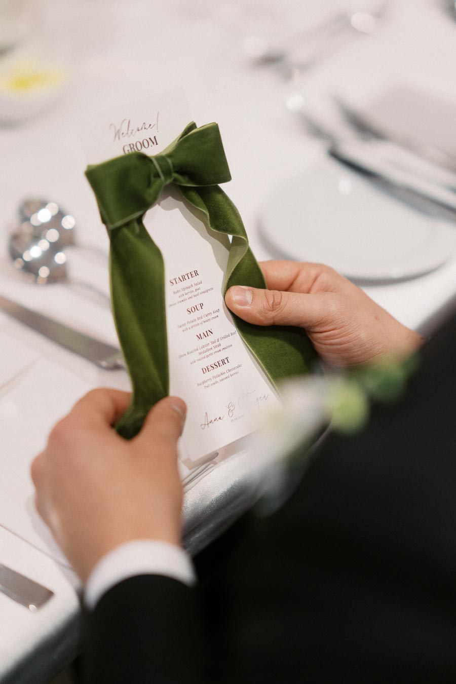 A person holding a wedding menu with a green bow, displaying courses like starter, soup, main, and dessert at a formal event.