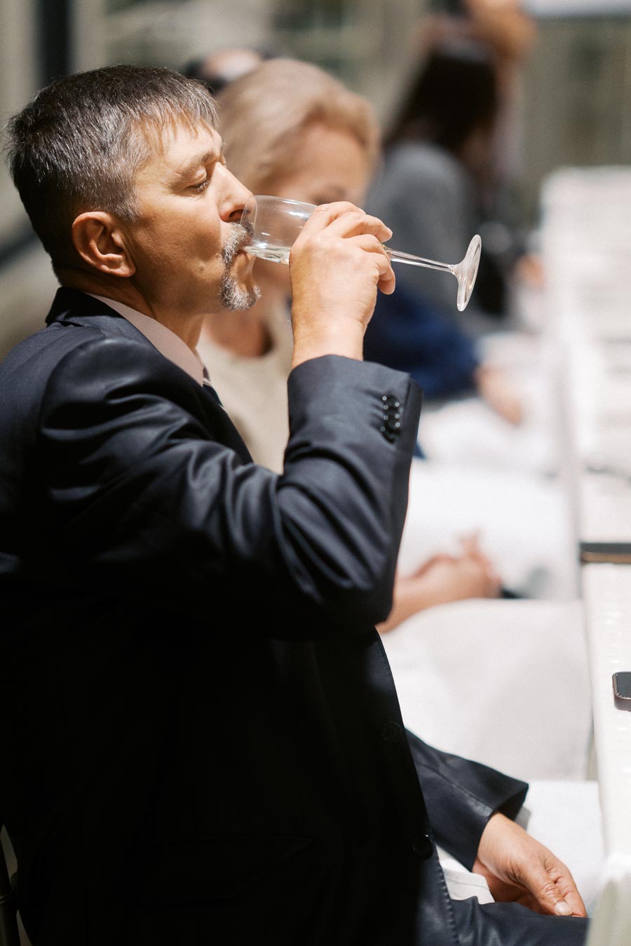 Man in a suit drinking from a wine glass at a formal event.