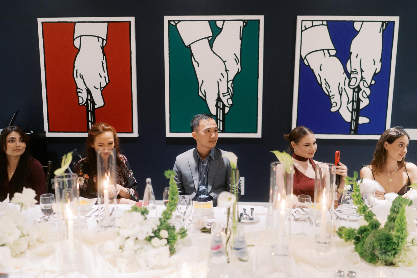 Group of people seated at an elegantly decorated dining table with contemporary art in the background, featuring vibrant red, green, and blue panels.