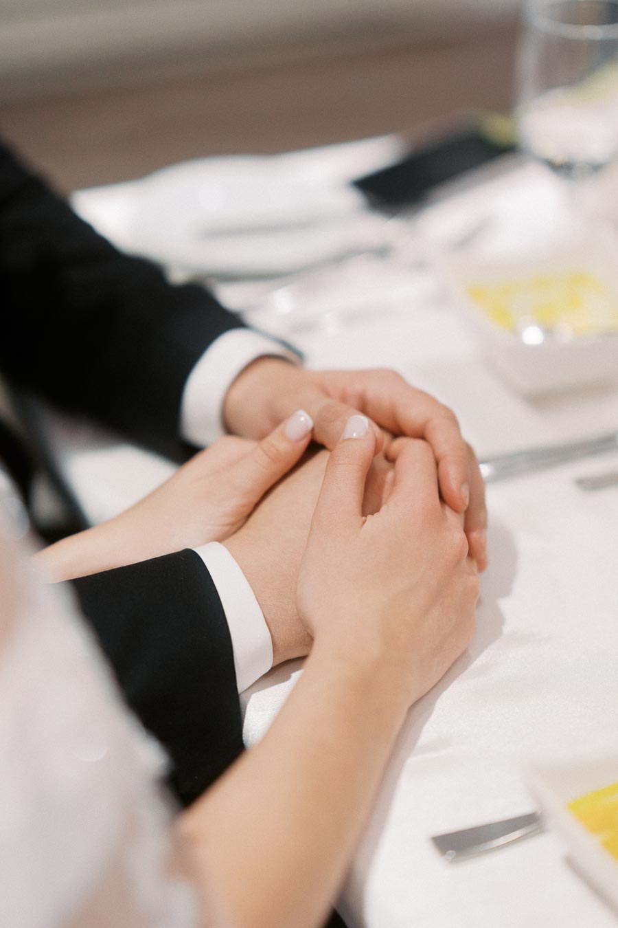 Couple holding hands at an elegant dining table, dressed in formal attire, showcasing love and connection.