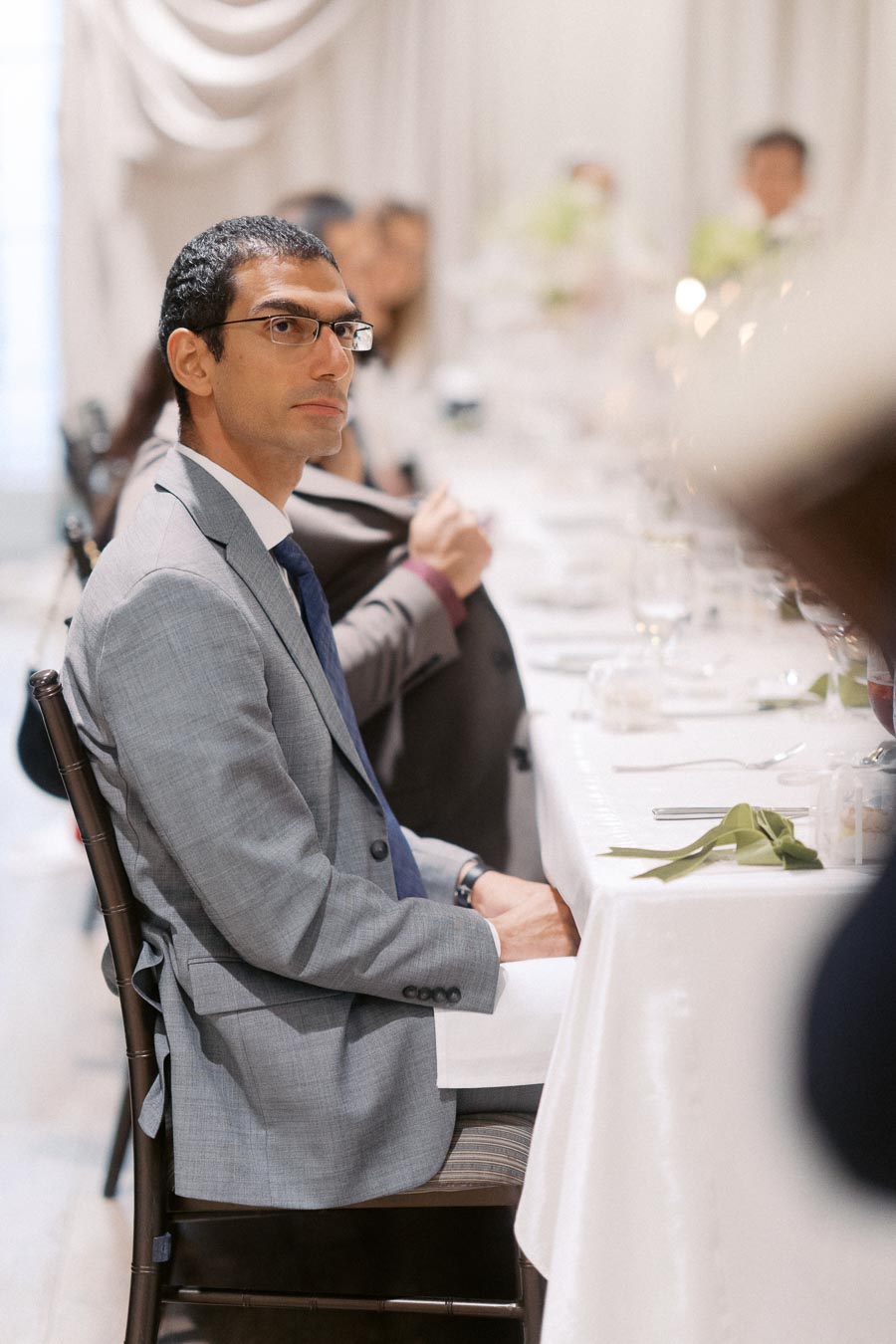 Man in a gray suit sitting at a formal dining table during an event.