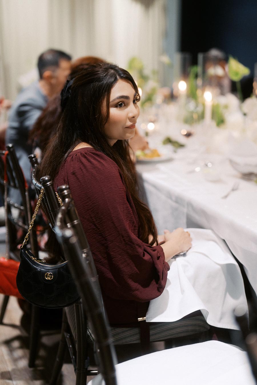 Young woman in elegant attire sitting at a beautifully set dinner table, indoors.