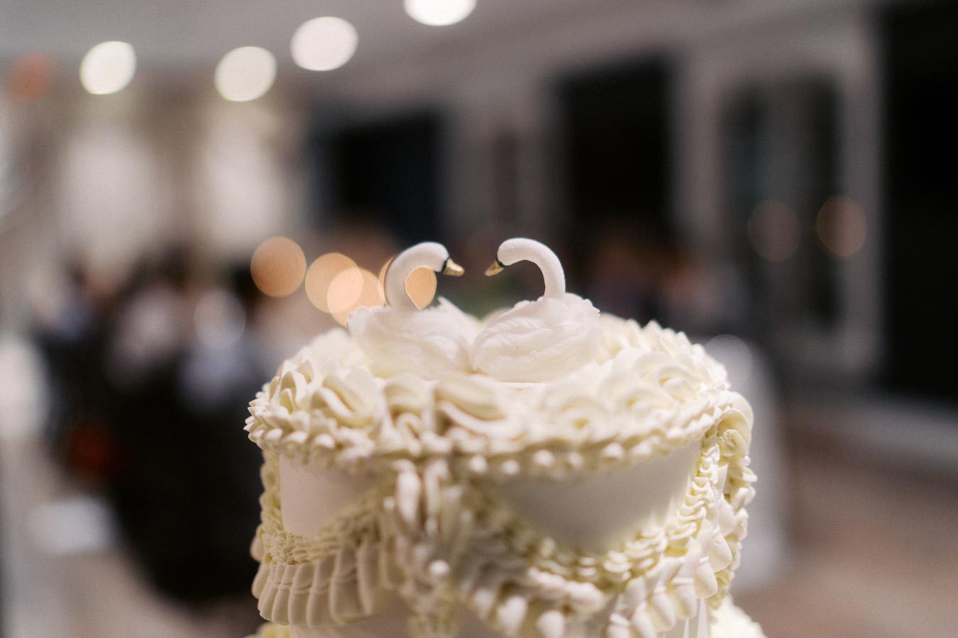 Elegant wedding cake with swan toppers, beautifully decorated with white frosting ruffles, perfect for a romantic celebration.