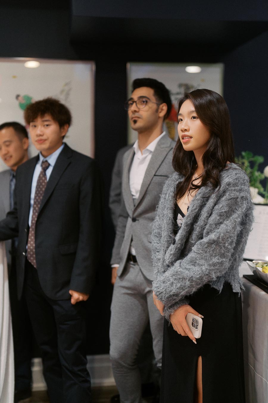 Group of professionals at a formal event, dressed in suits and elegant attire, standing indoors.