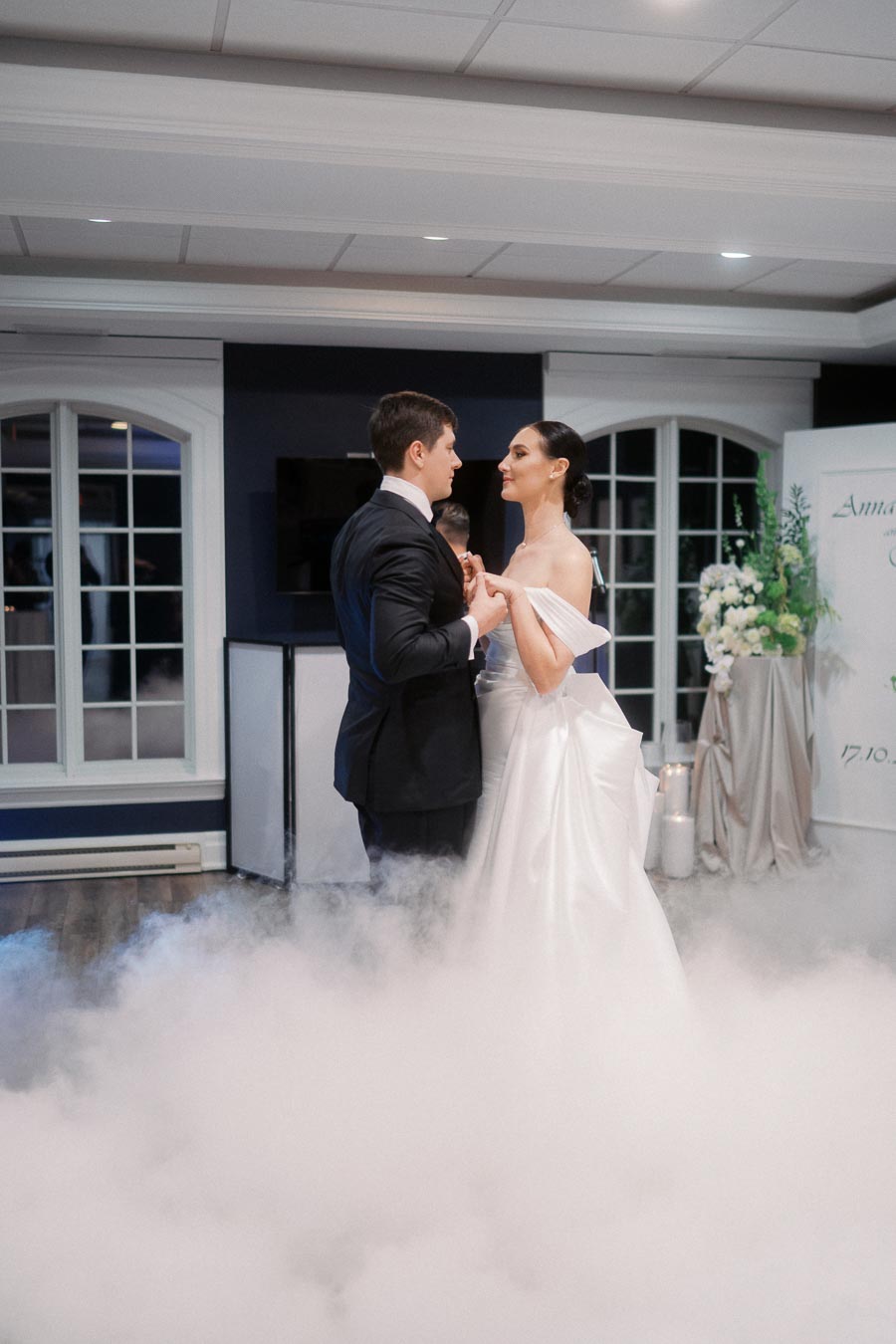 A bride and groom share a romantic dance surrounded by elegant decor and mist, highlighting their wedding celebration in a beautifully lit venue.