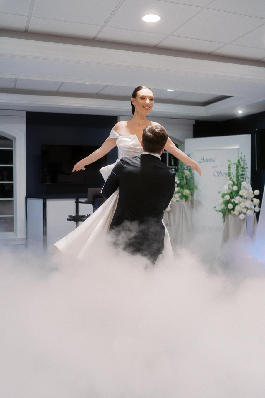 Bride and groom perform their first dance surrounded by smoke effects at an indoor wedding reception.
