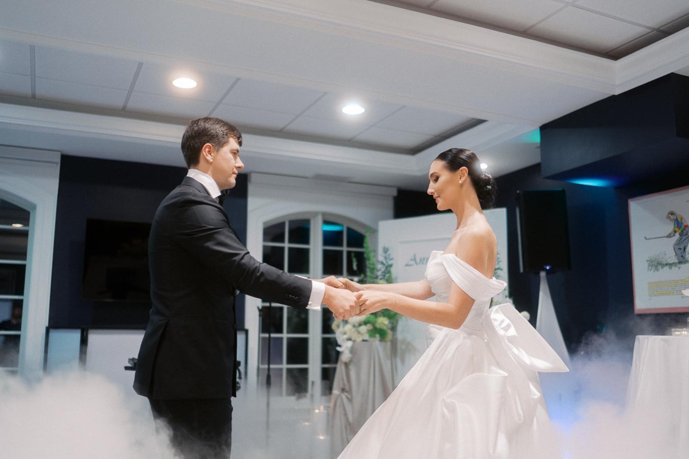 A bride and groom share a romantic first dance in an elegantly decorated venue, surrounded by soft lighting and mist, showcasing their formal wedding attire.