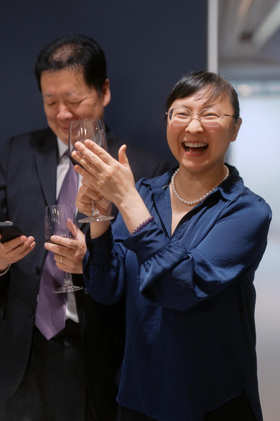 Two people enjoying a celebratory event, with one person laughing and holding a wine glass in an indoor setting.