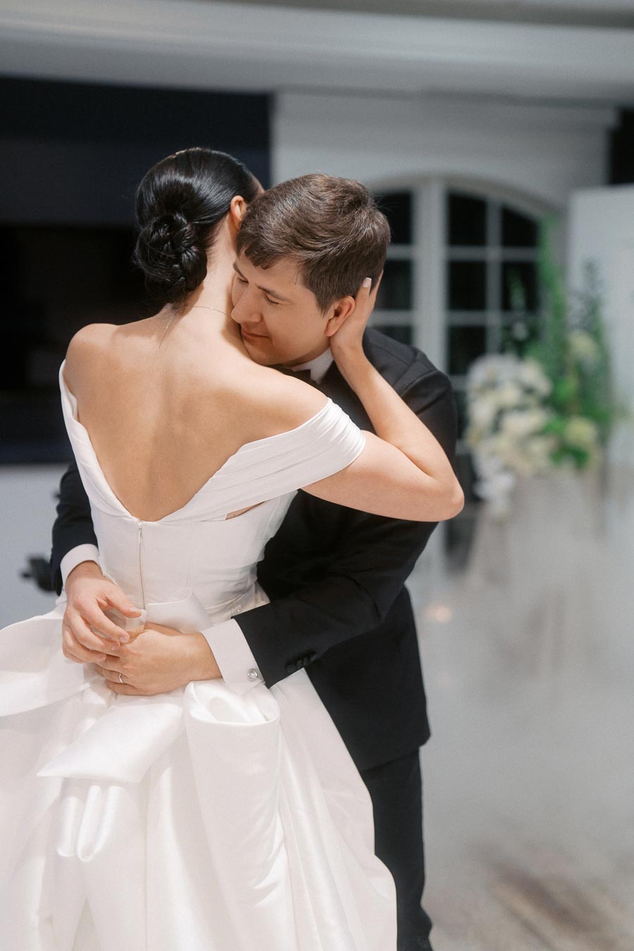 Bride and groom embrace during their wedding dance, showcasing elegant wedding attire and a romantic setting.