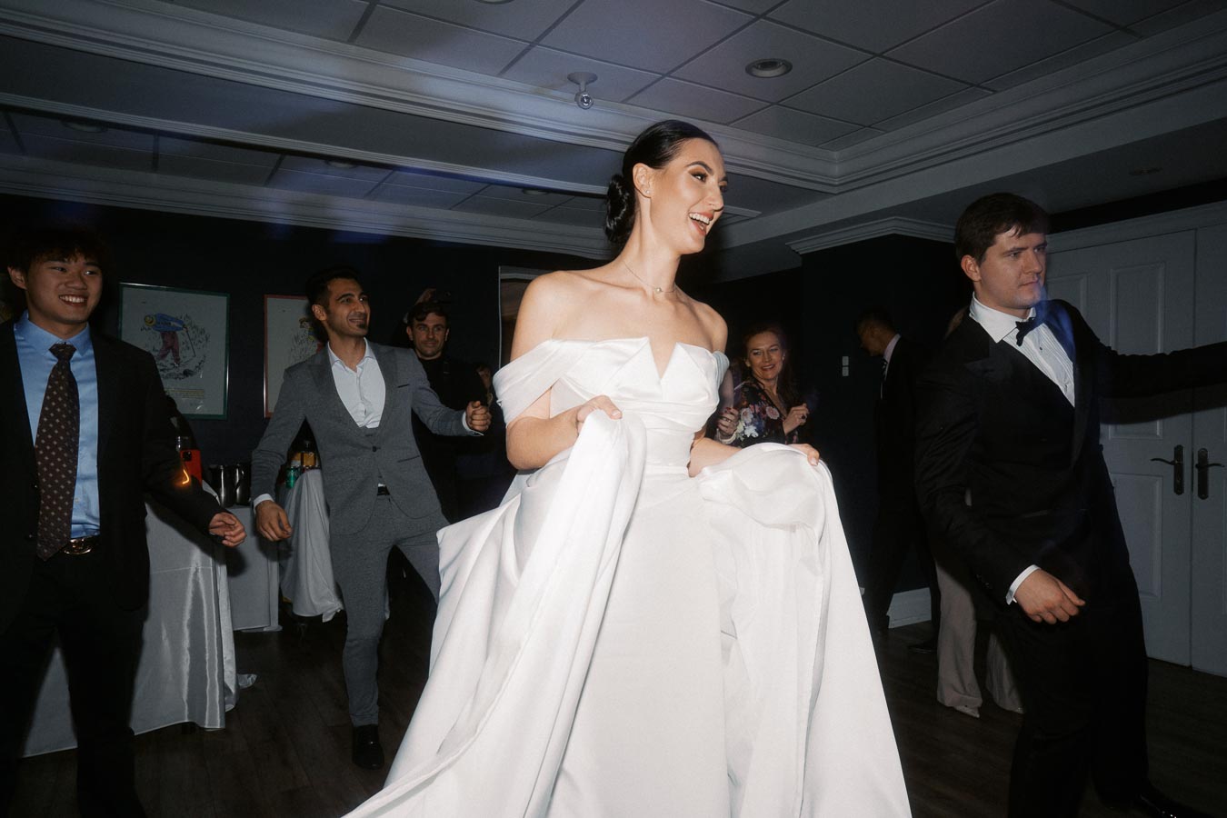 A joyful bride in a white gown dances with guests at a lively wedding reception.