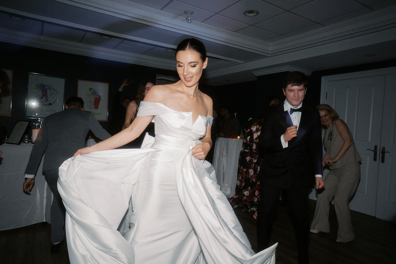 Bride in elegant white gown dancing at a wedding reception with guests in formal attire.