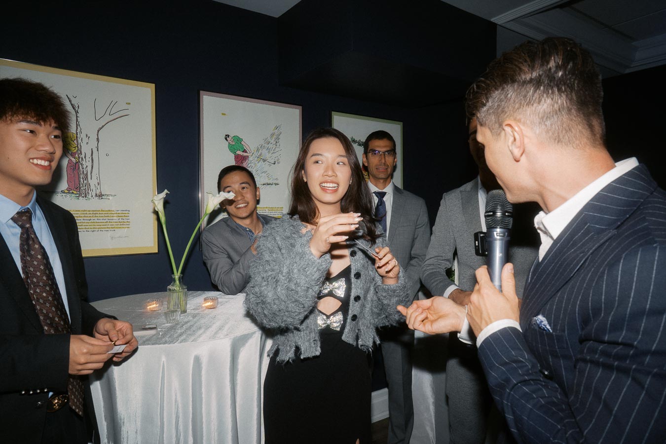 Group of people socializing at an event, with one person holding a microphone, having a conversation in a stylish, art-adorned room.
