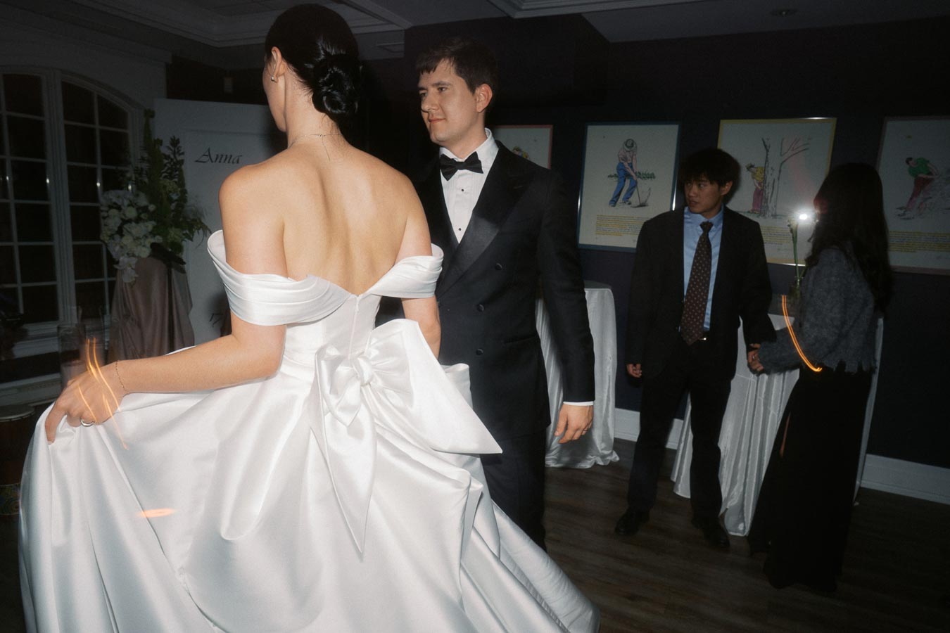 Elegant evening event with woman in a white gown and man in formal attire, captured in lively, upscale setting.