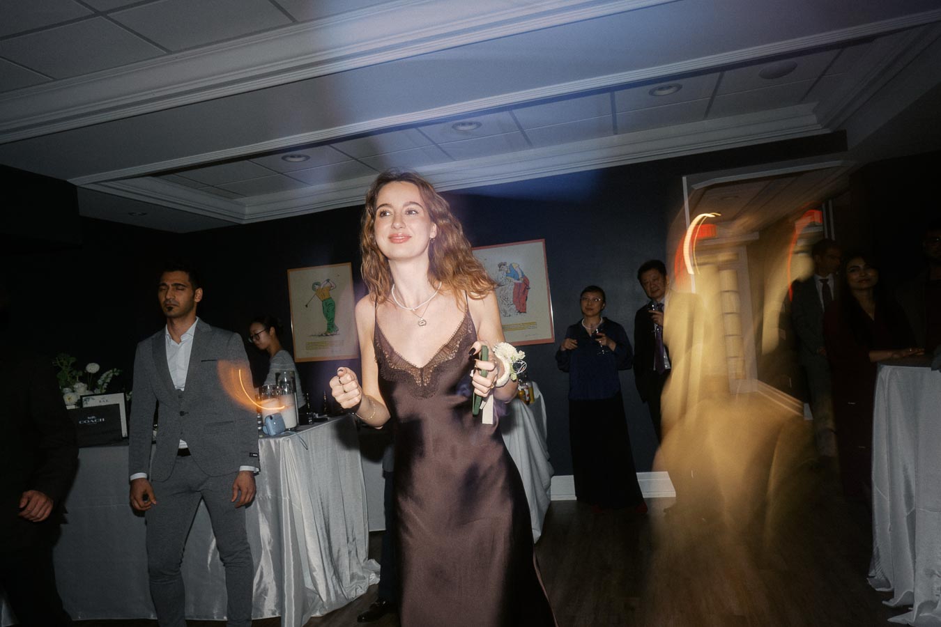 A woman in a brown dress enjoying a joyful moment on the dance floor at a social event, surrounded by other guests and a festive atmosphere.