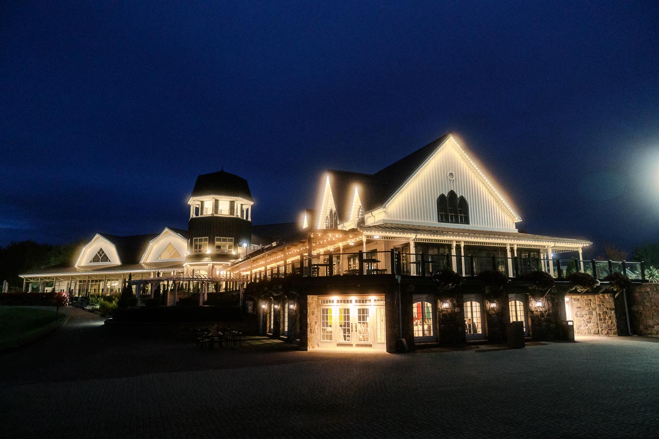 Illuminated country house at night with decorative lights, showing an inviting architectural design and serene ambiance against a deep blue evening sky.