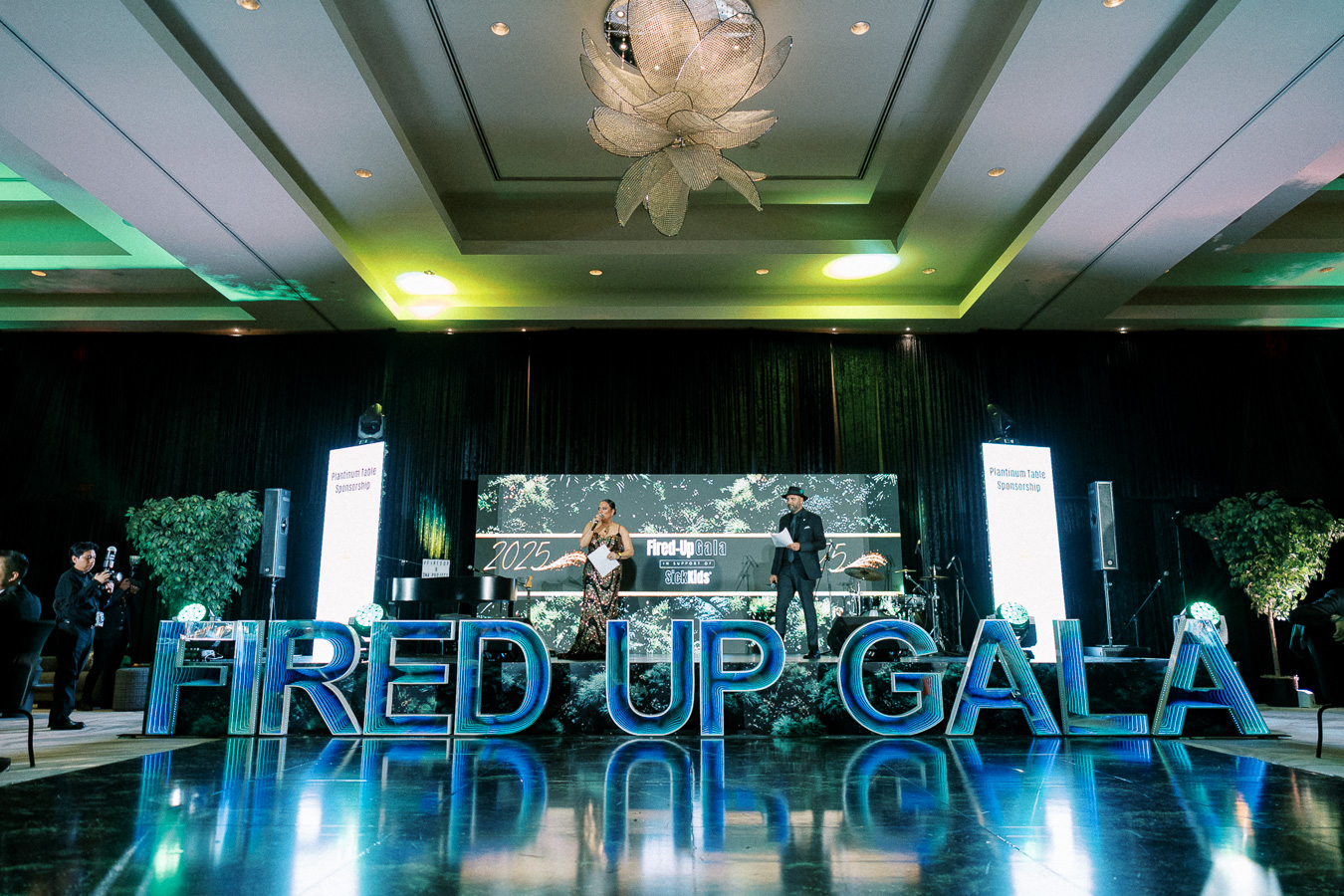 Elegant gala event showcasing large, illuminated Fired Up Gala letters with a stage set for speakers in a sophisticated venue, featuring modern lighting and decor.