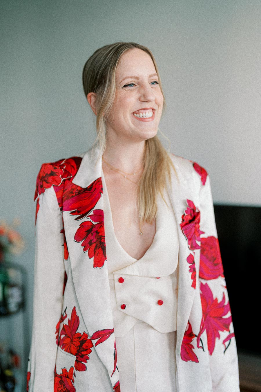 Smiling woman wearing a cream and red floral-patterned blazer against a neutral background.