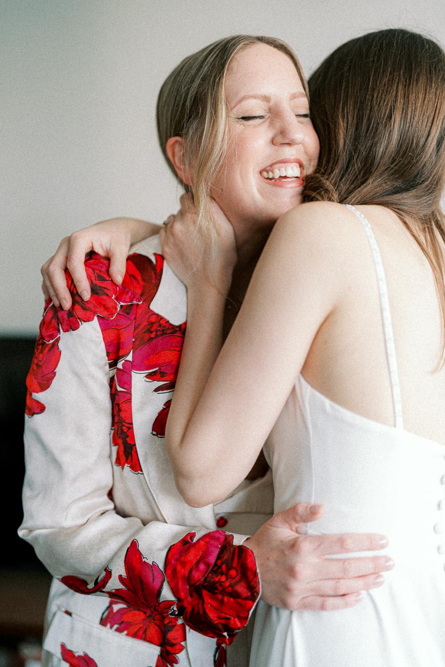 Two women sharing a joyful embrace, one wearing a white dress and the other in a floral-patterned outfit, highlighting a moment of happiness and friendship.