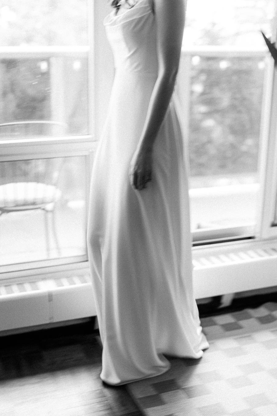 Elegant Woman in Flowing White Dress Near Bright Window - Black and White Photography.