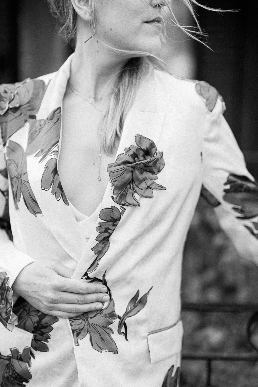 Black and white image of a person wearing a floral print blazer with the wind gently blowing their hair.