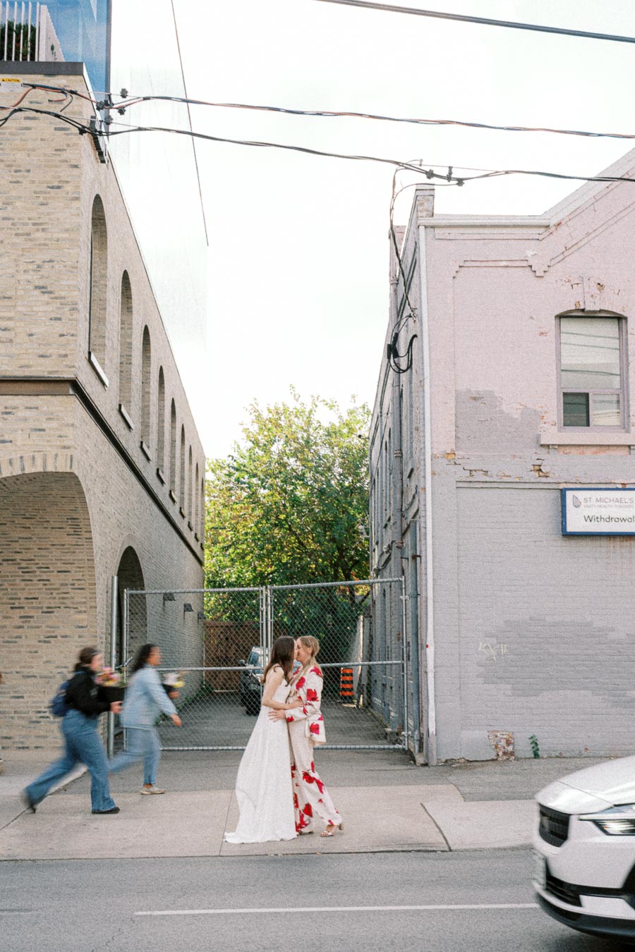 Romantic couple sharing a kiss on a city street, surrounded by blurred passersby and urban buildings.