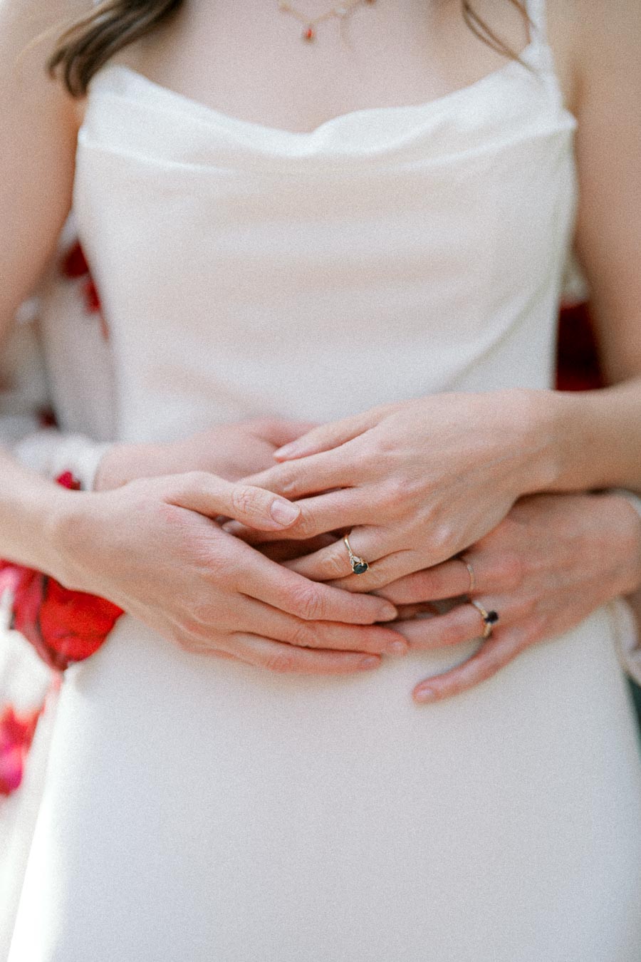 Close-up of couple embracing, showing intertwined hands with elegant rings on a white dress background, symbolizing love and commitment.