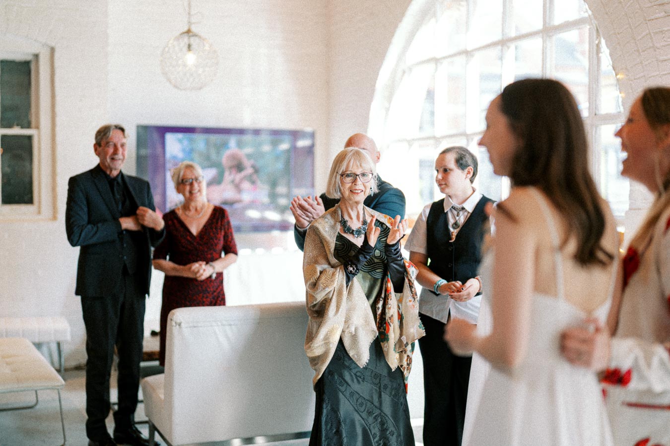 A joyful group of elegantly dressed people enjoying a celebration inside a stylishly decorated room with arched windows and modern lighting.