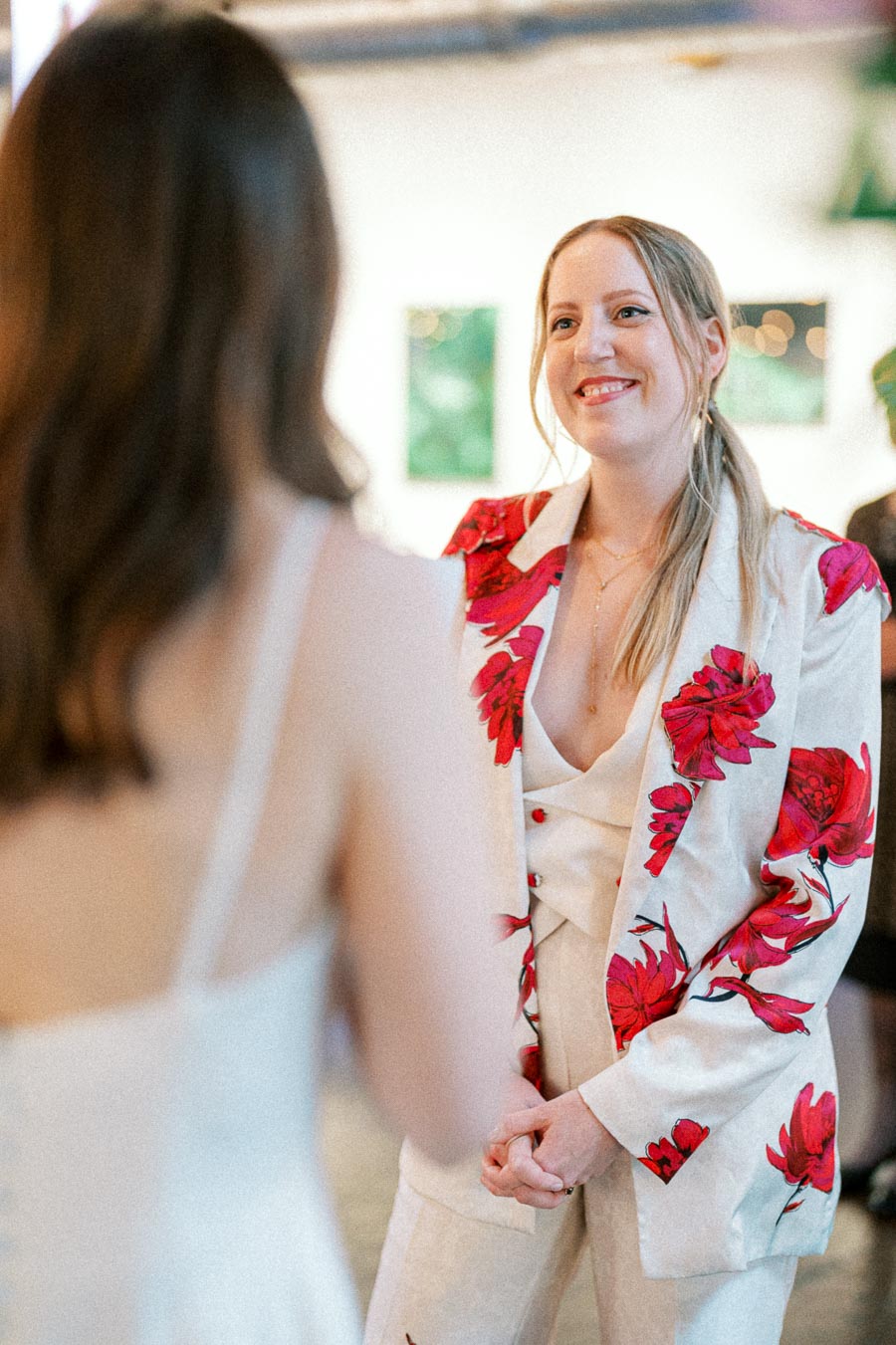 Young woman wearing a floral-patterned suit smiling at another person at an indoor event.