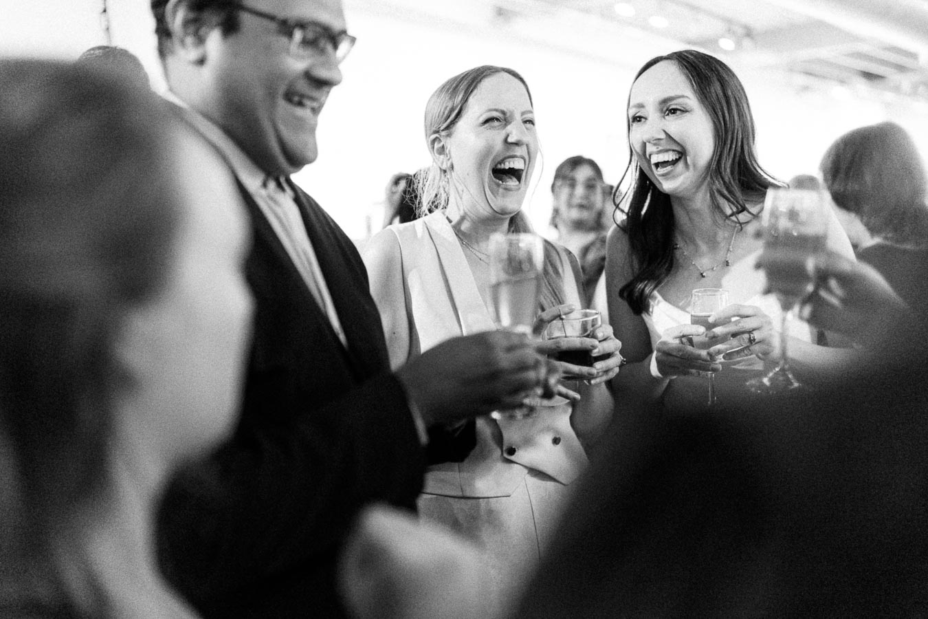 A group of people at a celebration, engaged in joyful laughter while holding drinks, creating a lively and festive atmosphere.