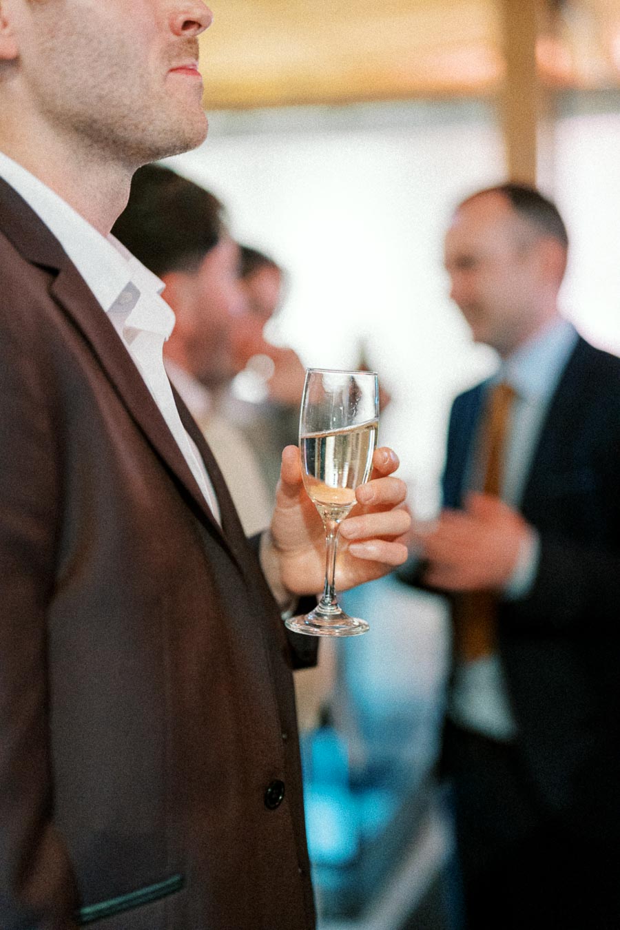 Man in a brown suit holding a champagne glass at a formal event.
