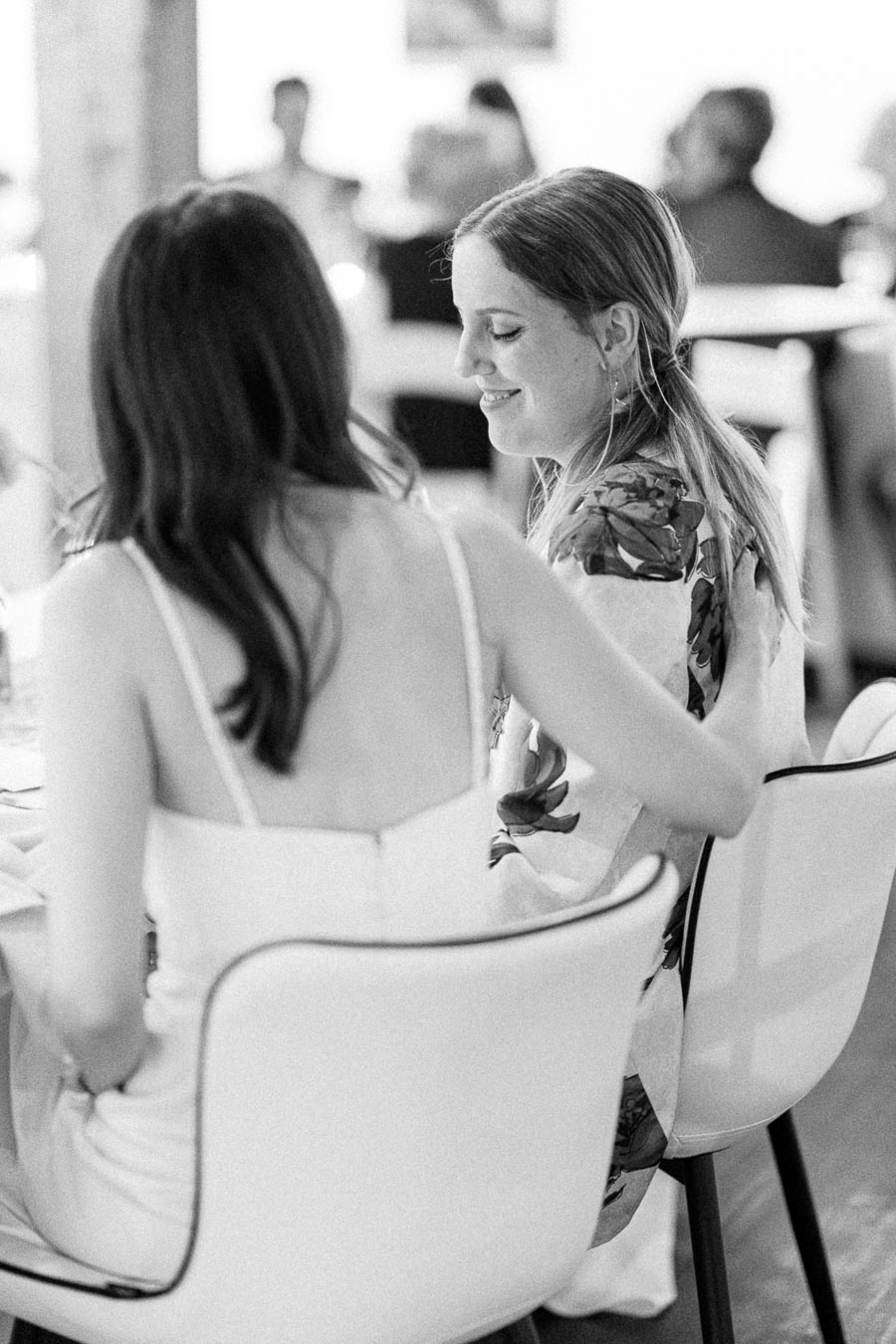Black and white photo of two women seated at a formal event, engaged in conversation, with soft lighting and elegant attire.