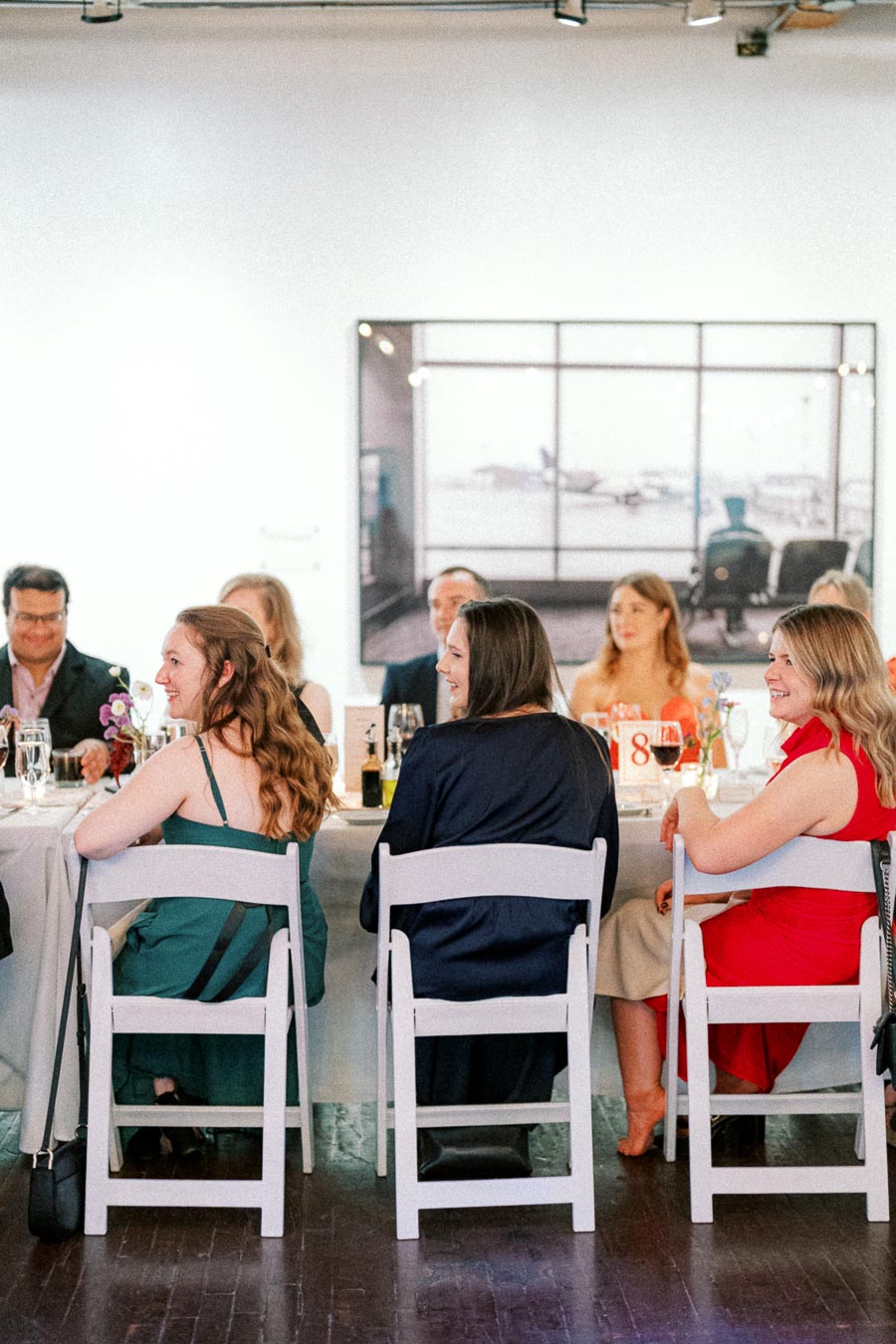 Group of people seated at a formal event, wearing elegant attire, engaged in conversation and enjoying a meal at a well-decorated table.