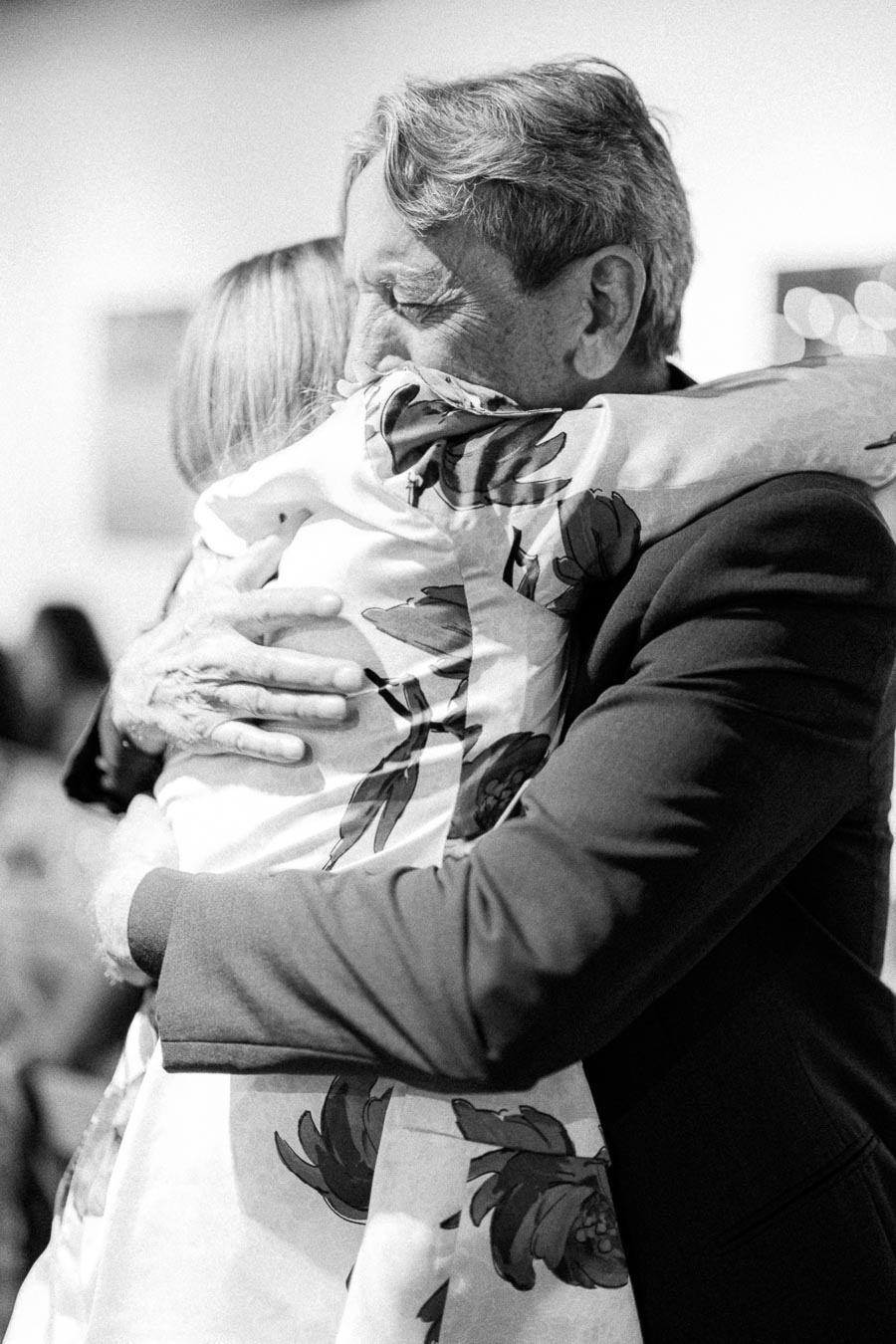Black and white image of two people hugging warmly, one wearing a floral-patterned garment, conveying a sense of comfort and connection.
