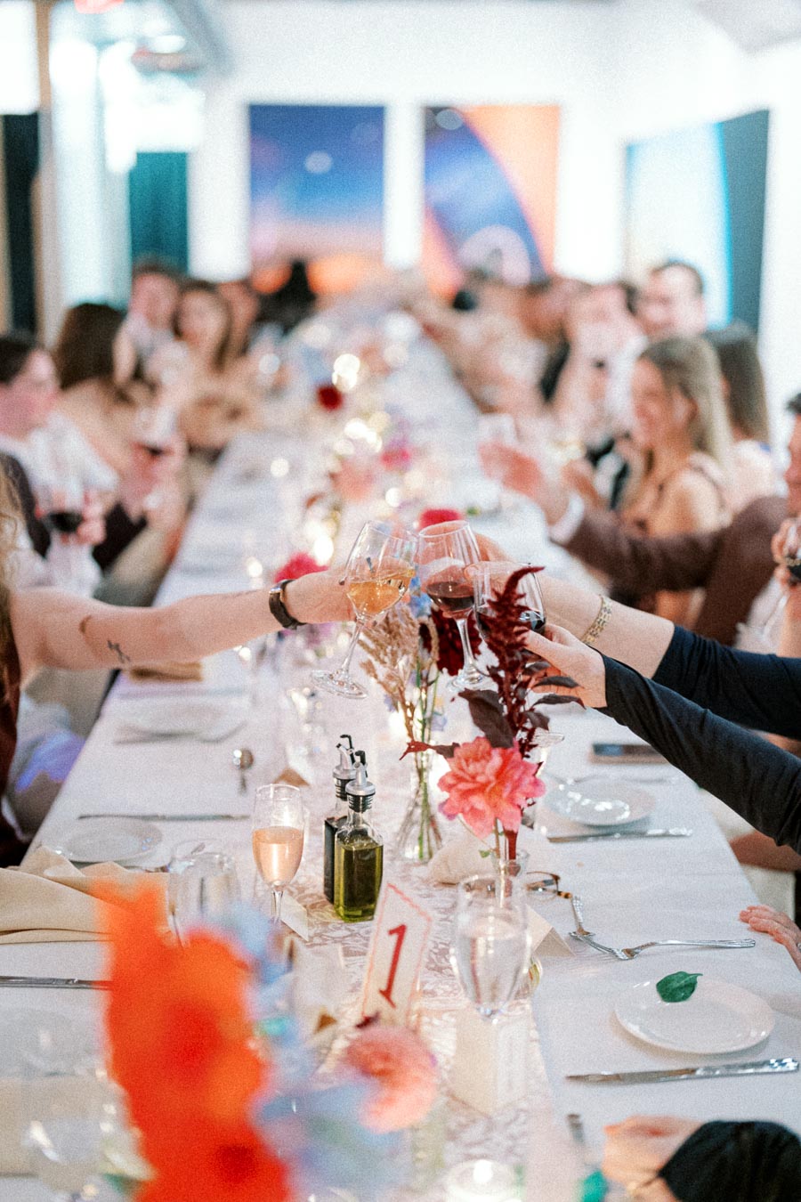 Elegant dinner party setting with a long, beautifully decorated table featuring floral arrangements and people raising glasses for a toast, creating a festive and joyful atmosphere.