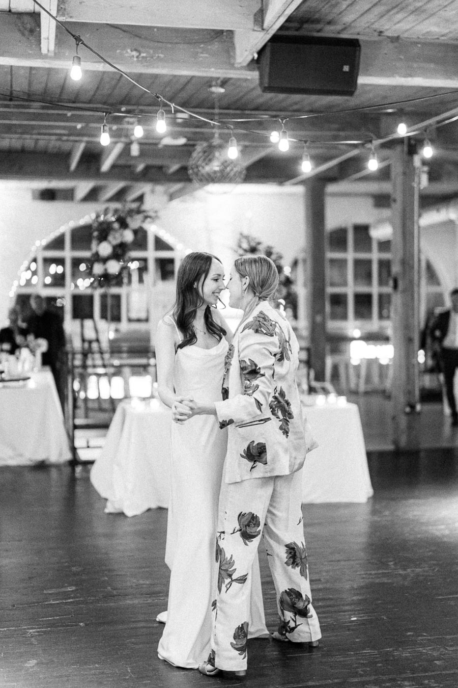 Elegant black and white photo of a couple dancing at their wedding reception, with romantic string lights creating an intimate atmosphere in a stylish venue.