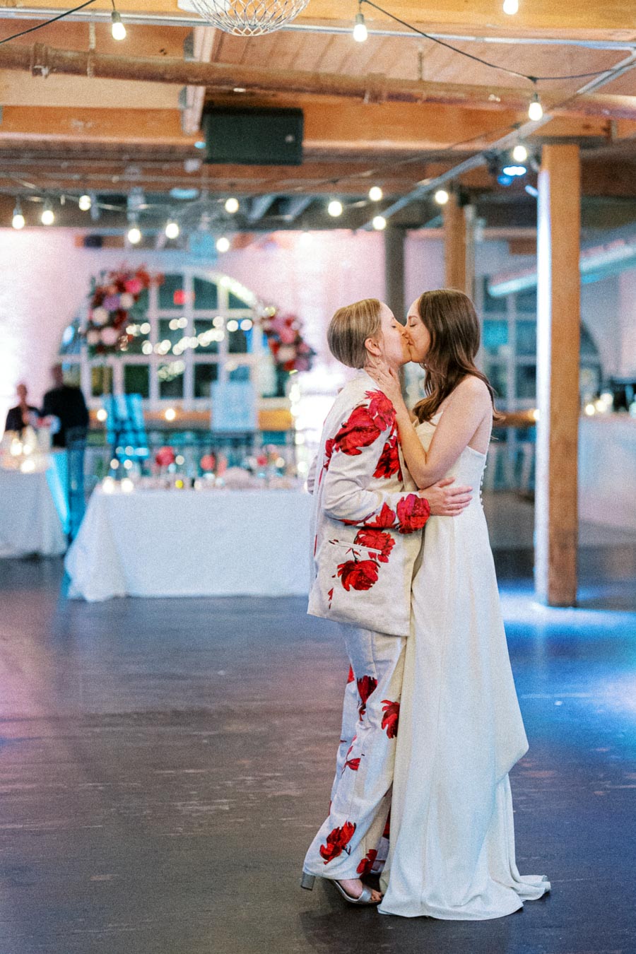 Romantic wedding moment of a couple sharing a kiss in an elegantly decorated venue with floral arrangements and soft lighting.