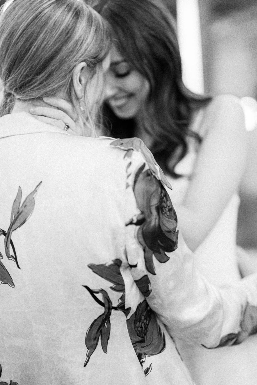 Romantic black and white photograph of two women embracing, one wearing a floral-patterned garment.