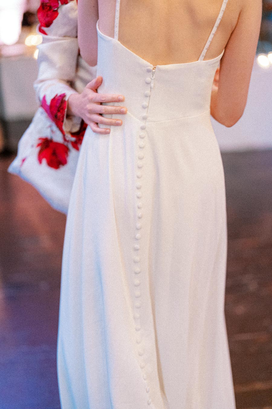 Elegant back of a white wedding dress with button detailing, worn by a person embraced by another in a floral-patterned outfit.