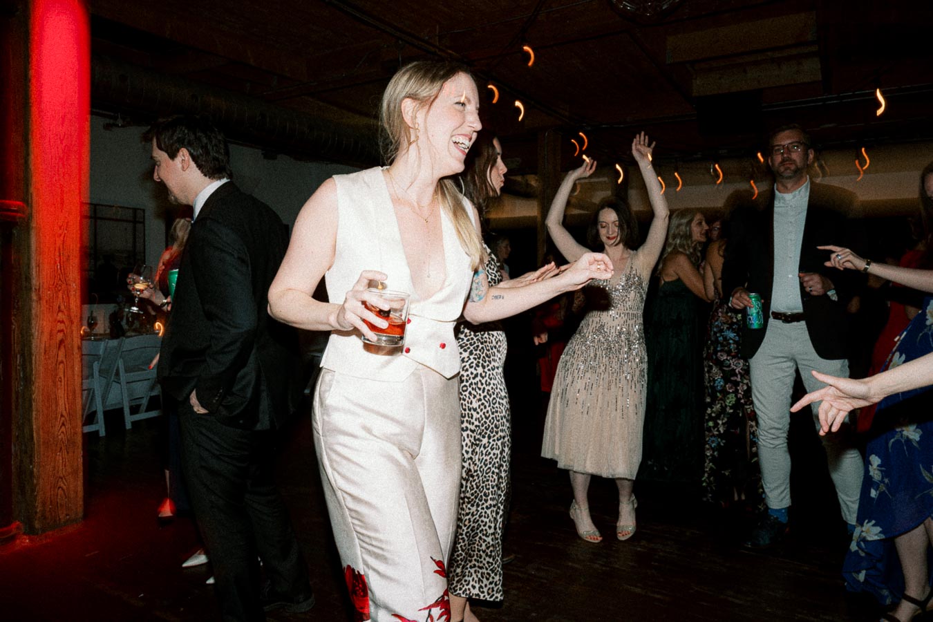 A group of elegantly dressed adults dancing and enjoying a party in a dimly lit room with a lively atmosphere.