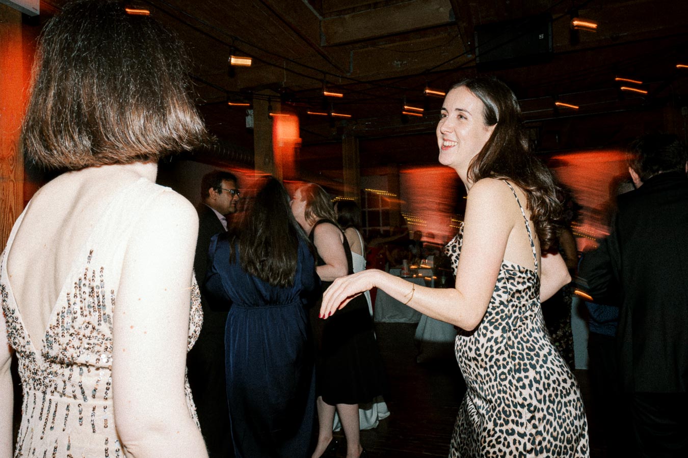 Elegant evening party scene with people dancing in stylish dresses, capturing a joyful and lively atmosphere with warm lighting and wood-paneled surroundings.