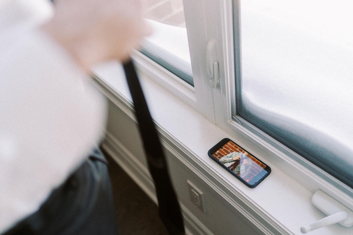 Smartphone displaying video resting on a snowy windowsill indoors near a blurred figure.
