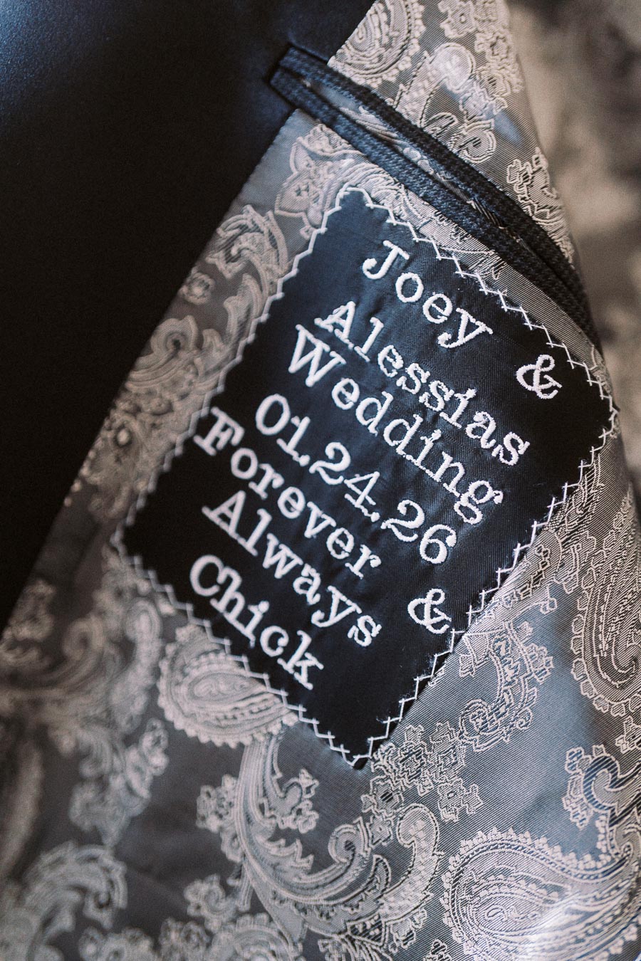 Close-up of personalized wedding jacket interior with embroidered message Joey & Alessia's Wedding 01.24.26 Forever & Always on paisley pattern fabric.
