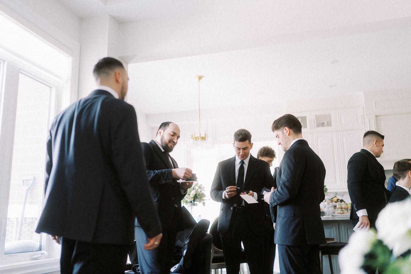 A group of men in suits gather in a bright, modern room, likely preparing for a formal event or meeting.