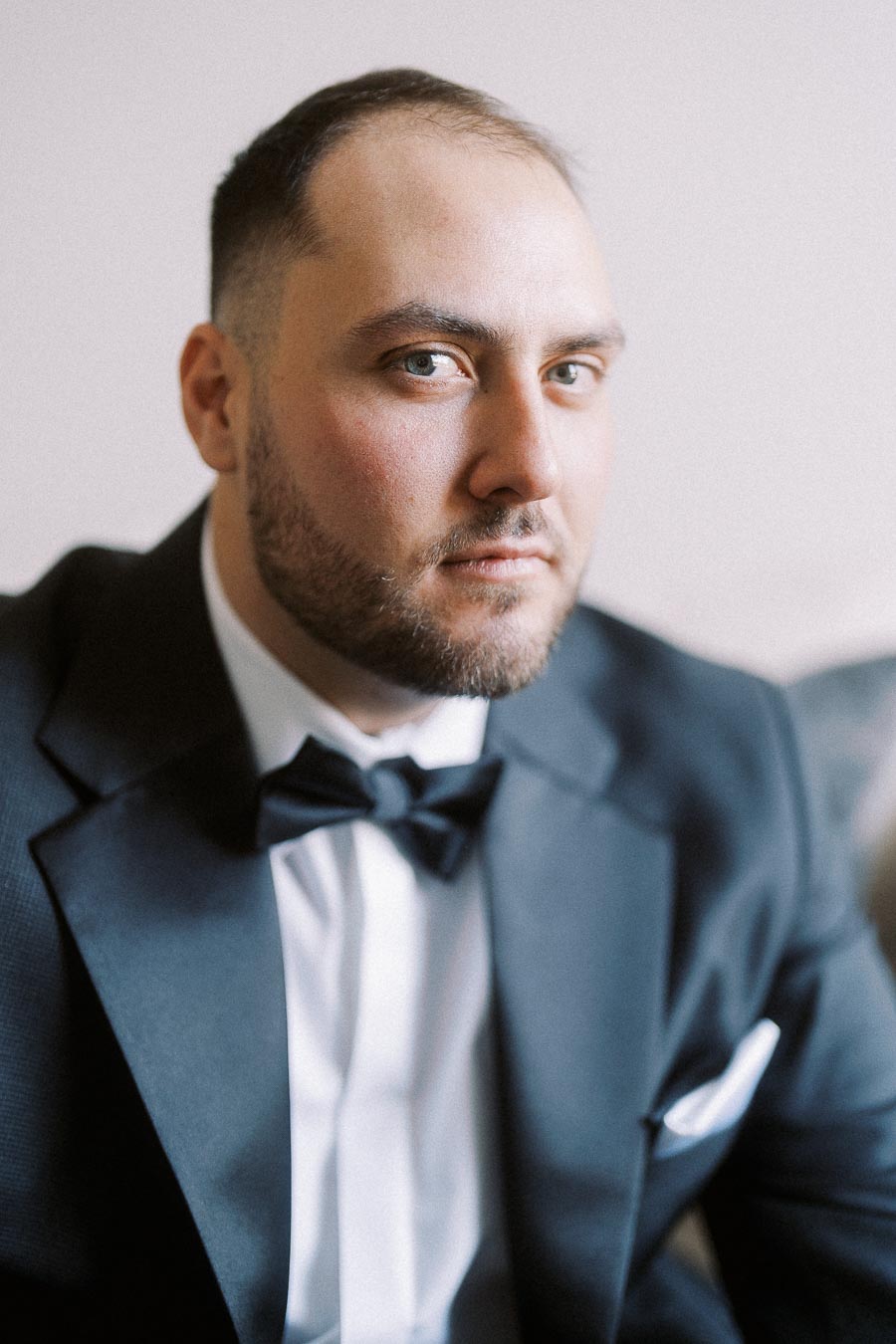 A man wearing a formal black tuxedo and bow tie, posing for a professional portrait with a focused expression.