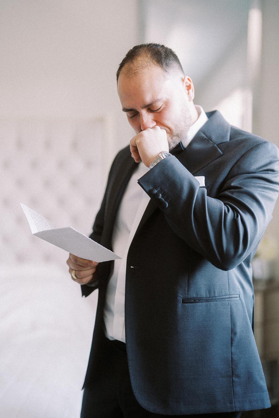 Man in a suit reading a letter with an emotional expression, reflecting a moment of deep contemplation or sentimentality.